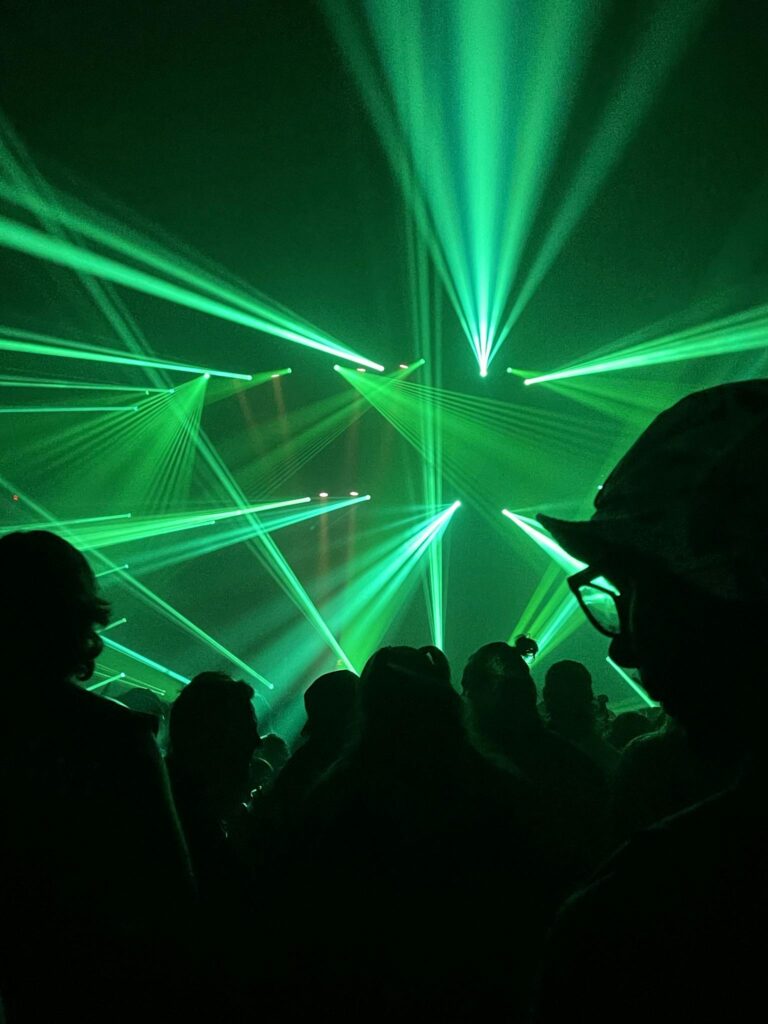 Vibrant green laser beams illuminate the night at an energetic concert or rave, creating a futuristic atmosphere.